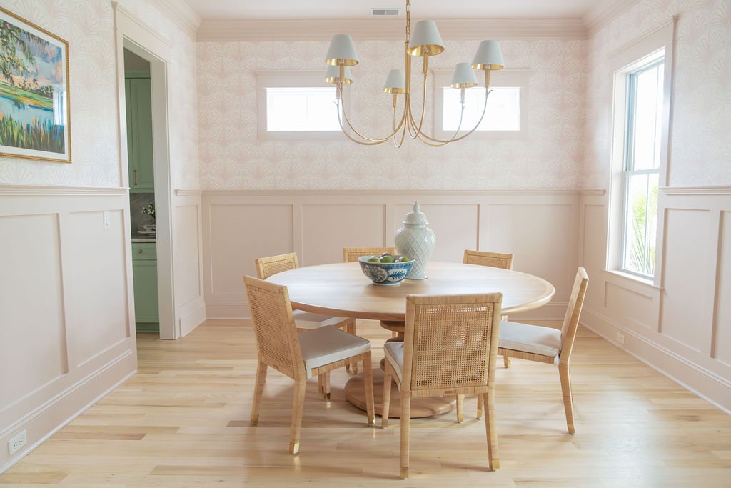 Pink wallpapered dining room with a round table and brass chandelier